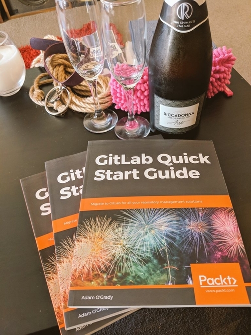 Three copies of GitLab Quick Start Guide by Adam O’Grady on the coffee table with champagne and rope