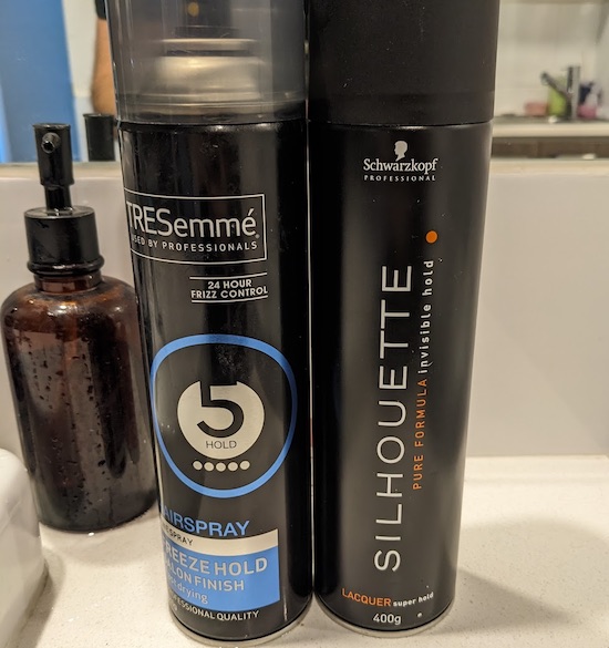 Two large cans of hairspray on a bathroom vanity.